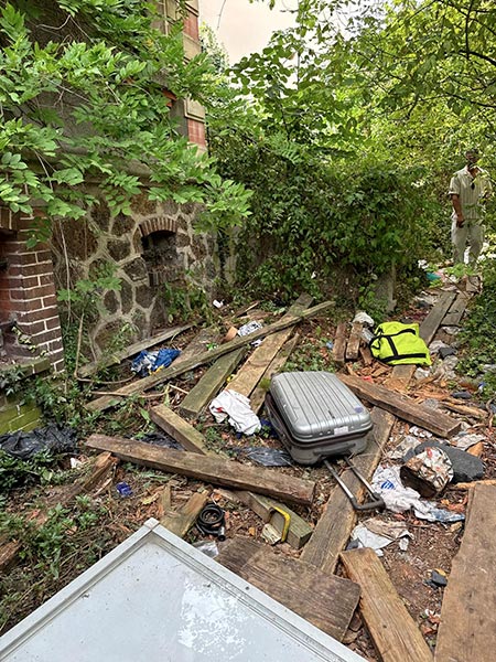 Jardin encombré de bois, valises et déchets avant une intervention de débarras