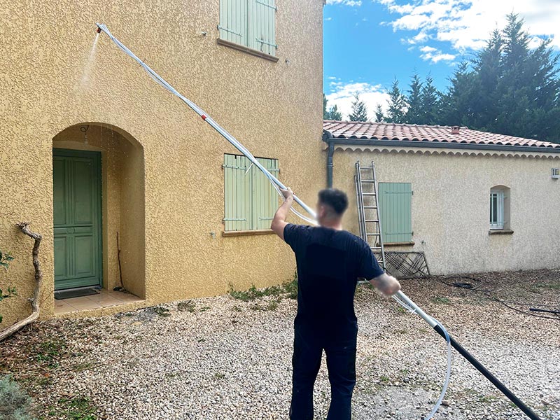 photo du technicien en plein nettoyage au karcher de la façade encrassé de maison